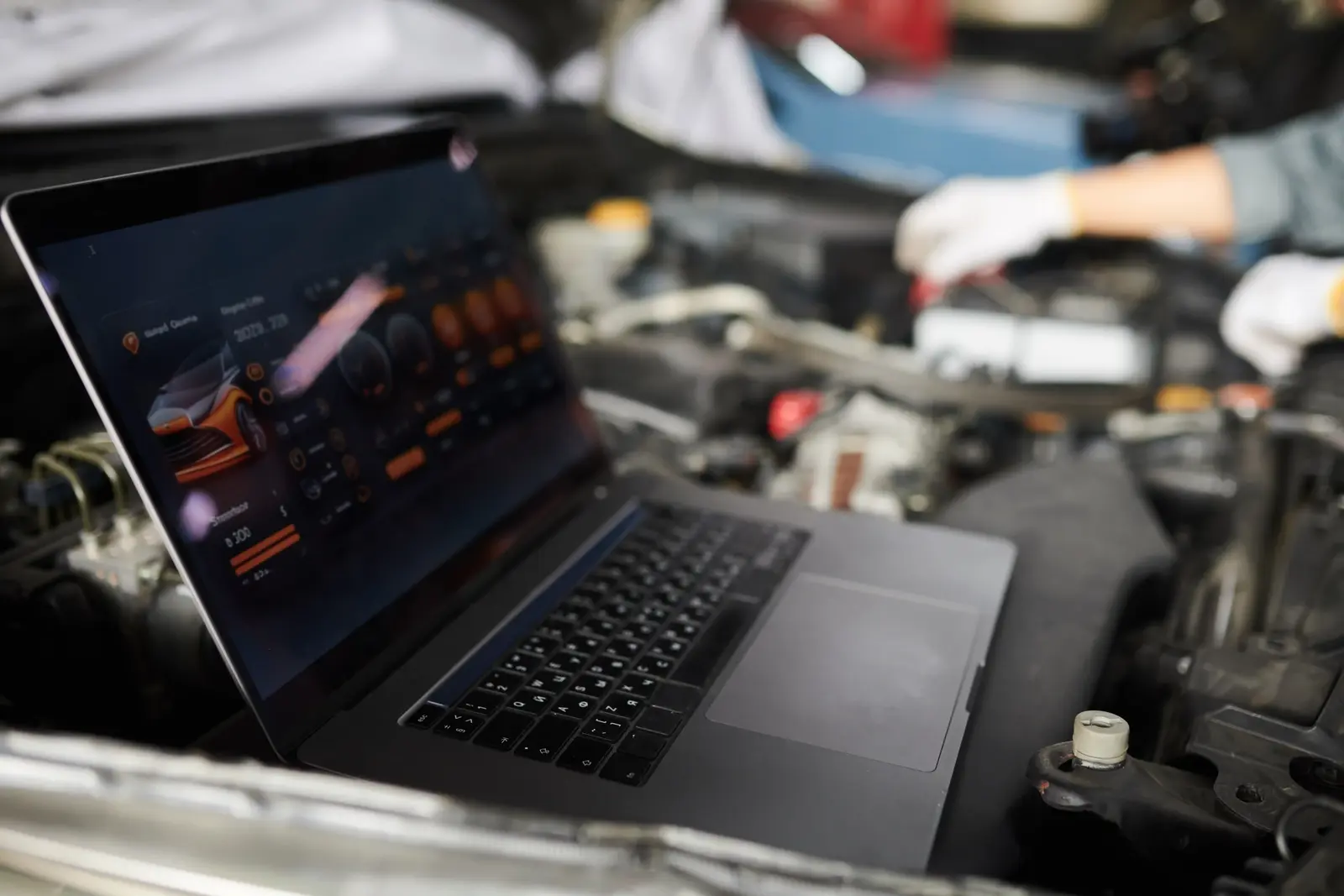 Laptop running ECU tuning software resting on a car’s engine bay while a gloved mechanic connects leads during a mobile remap.